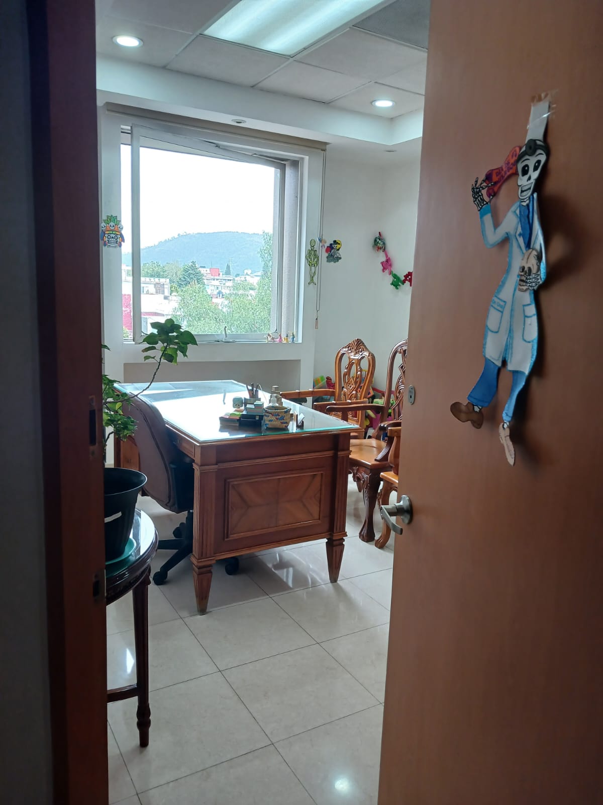 Puerta del consultorio decorada con una calaverita artesanal vestida de doctor, con el escritorio al fondo