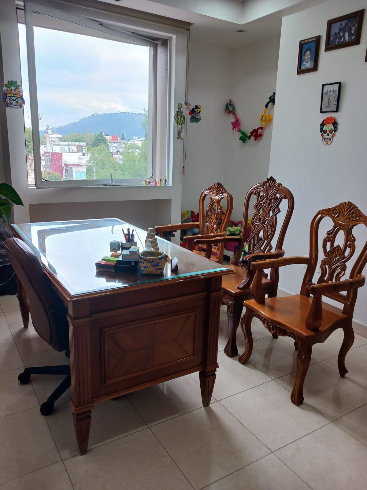 Consultorio de la Mtra. Lenia con escritorio de madera, sillas talladas, juguetes en un rincón y una ventana con vista a las montañas